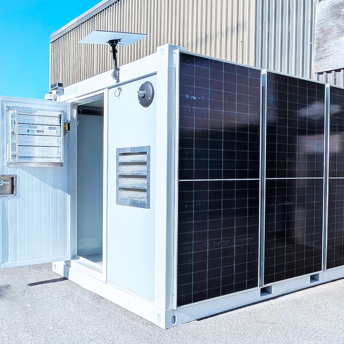 Angled view of Li-Cube Power12 container entrance with open door, electrical panel, and solar panels on the side wall